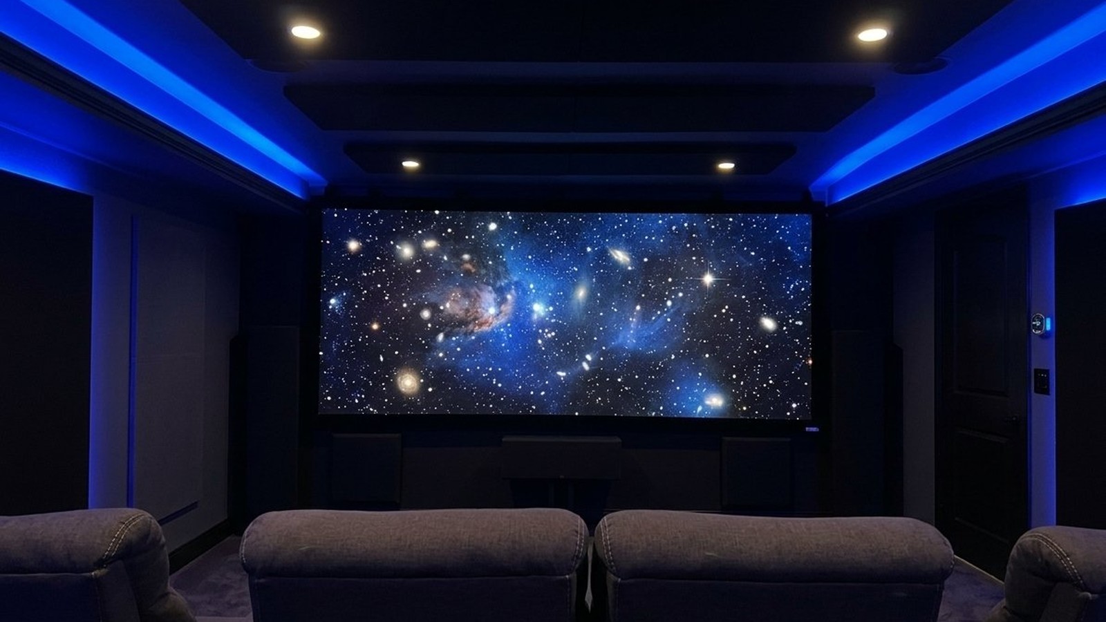 Salle de cinéma maison avec écran de projection, fauteuils inclinables et éclairage d'ambiance bleu